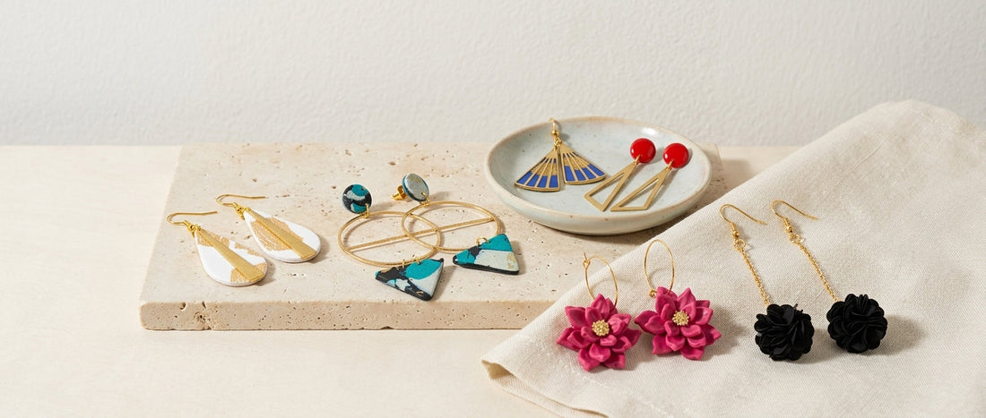 Handmade artisan earrings styled on a travertine stone slab, ceramic dish, and natural linen cloth.   