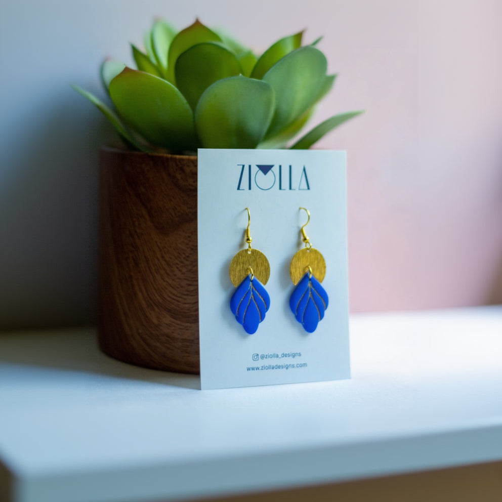 Blue and gold earrings on a Ziolla card with a plant in the background
