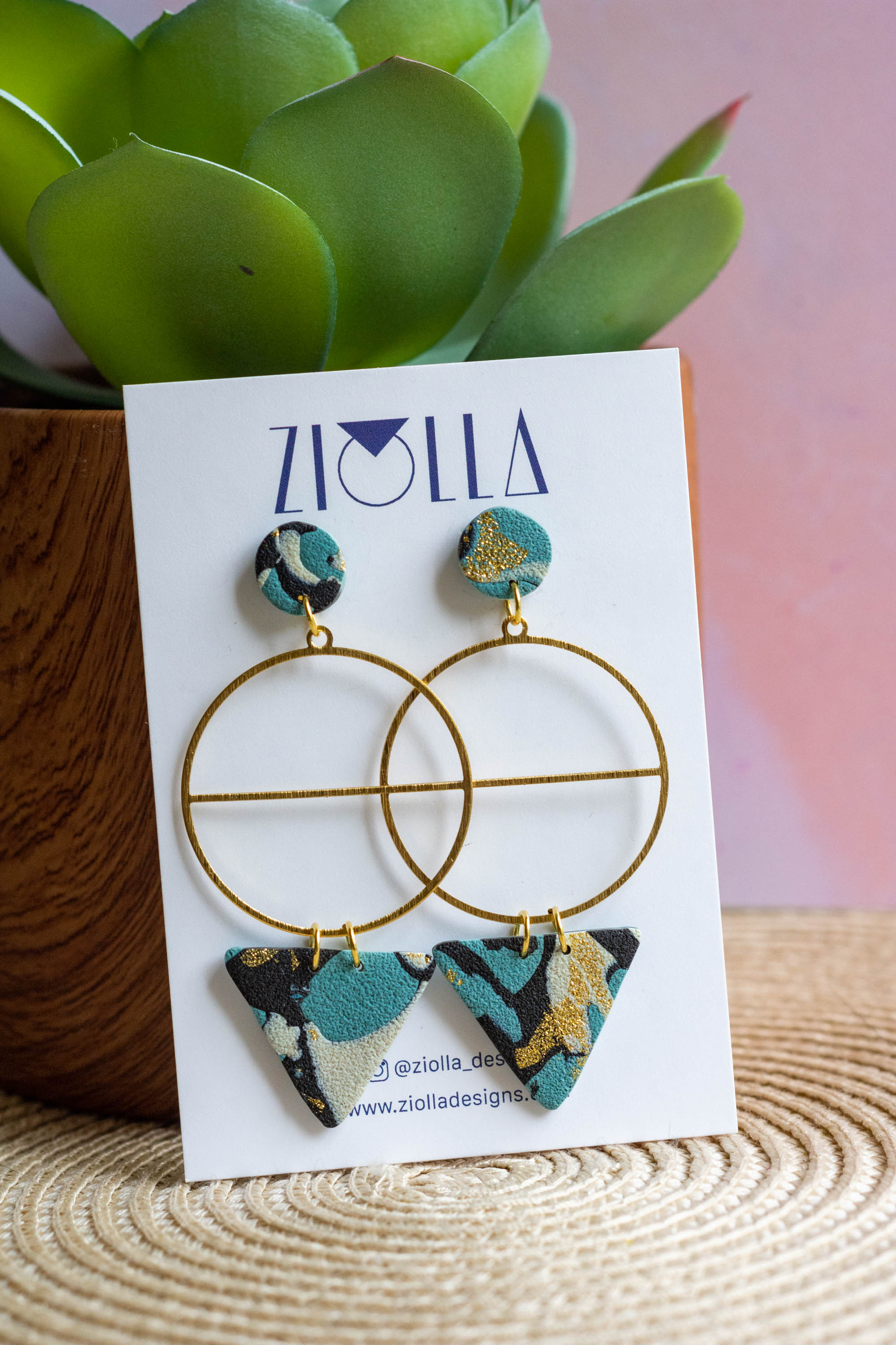 Handmade geometric statement earrings by Ziolla Designs, featuring gold-plated circular hoops with marbled teal, black and gold polymer clay details, displayed on a branded jewellery card.