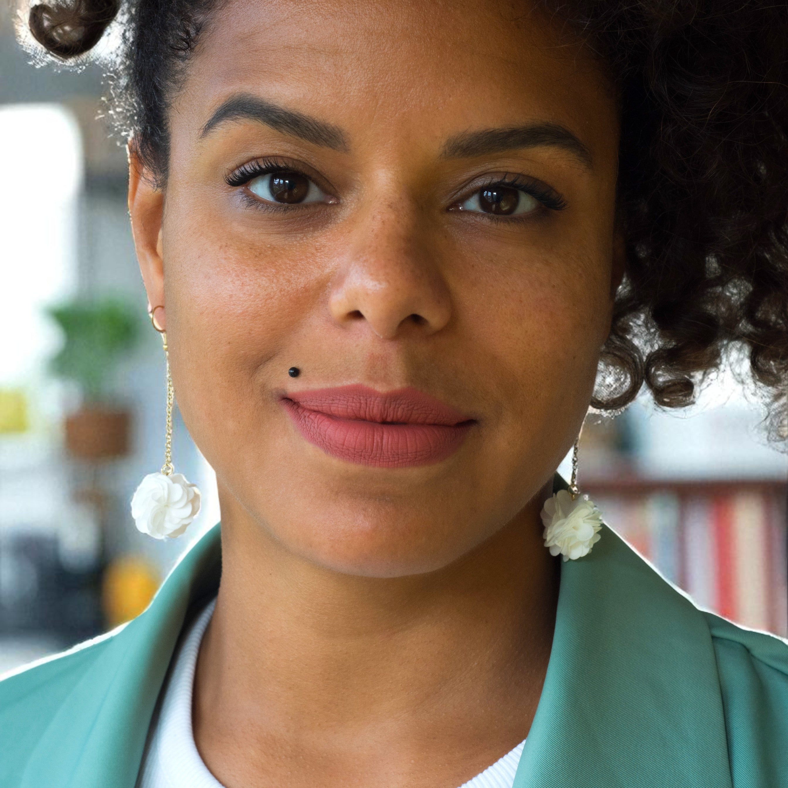 Woman with styled hair wearing earrings and a green jacket.