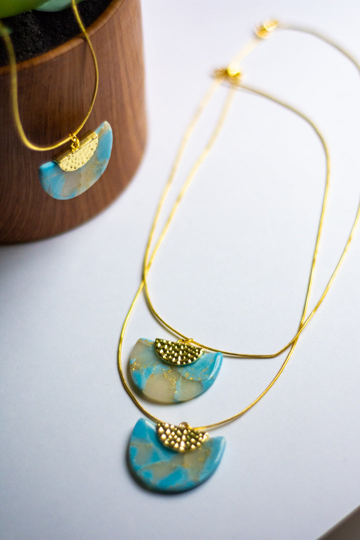 Gold necklaces with blue faux stone pendants on a white surface