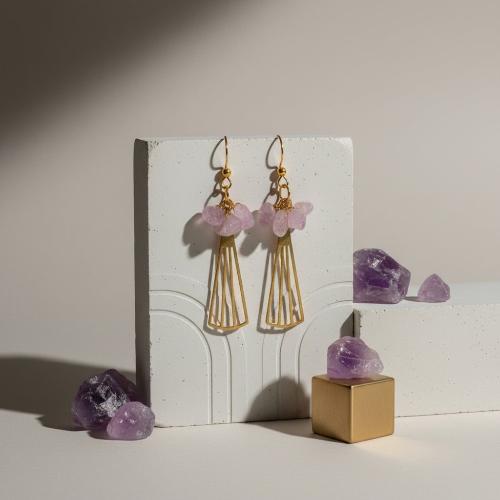 Gold earrings with pink gemstones on a white stand with amethyst crystals.