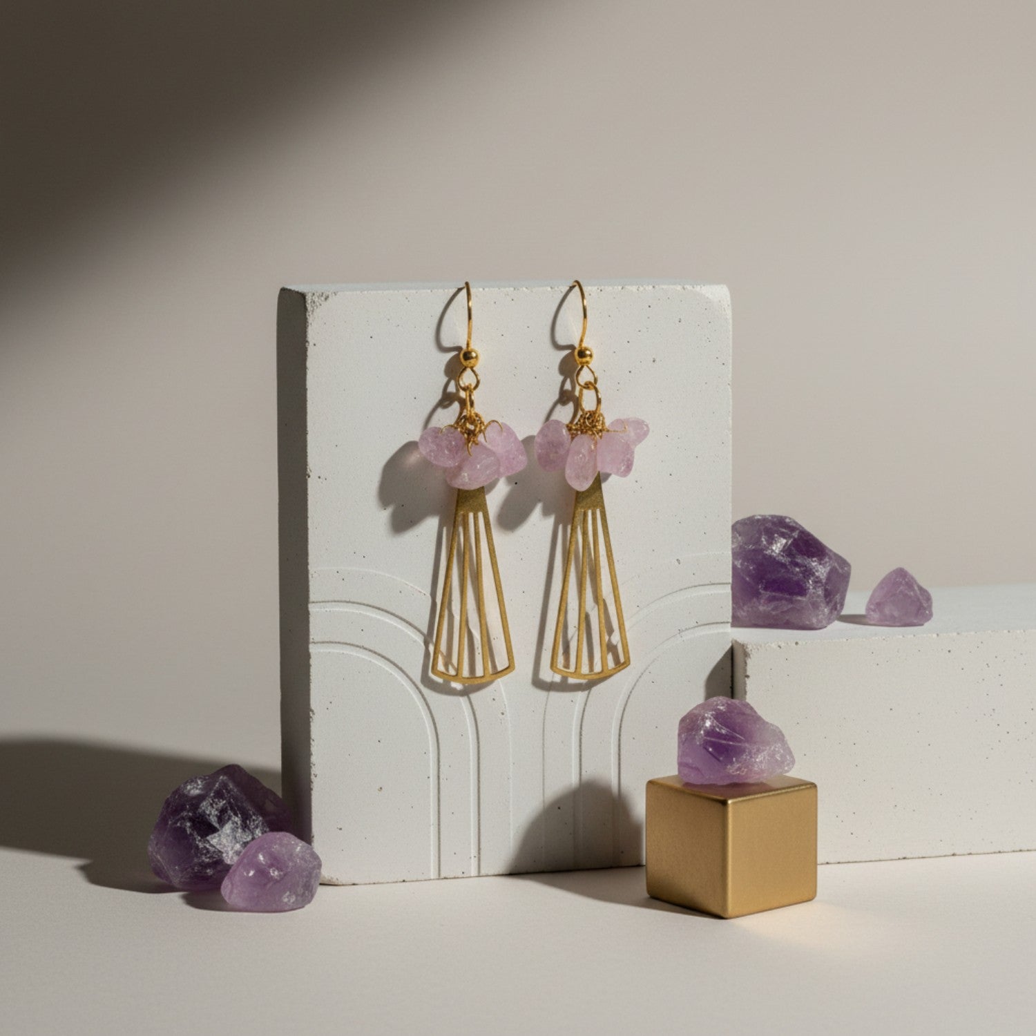 Gold earrings with pink gemstones on a white stand with amethyst crystals.