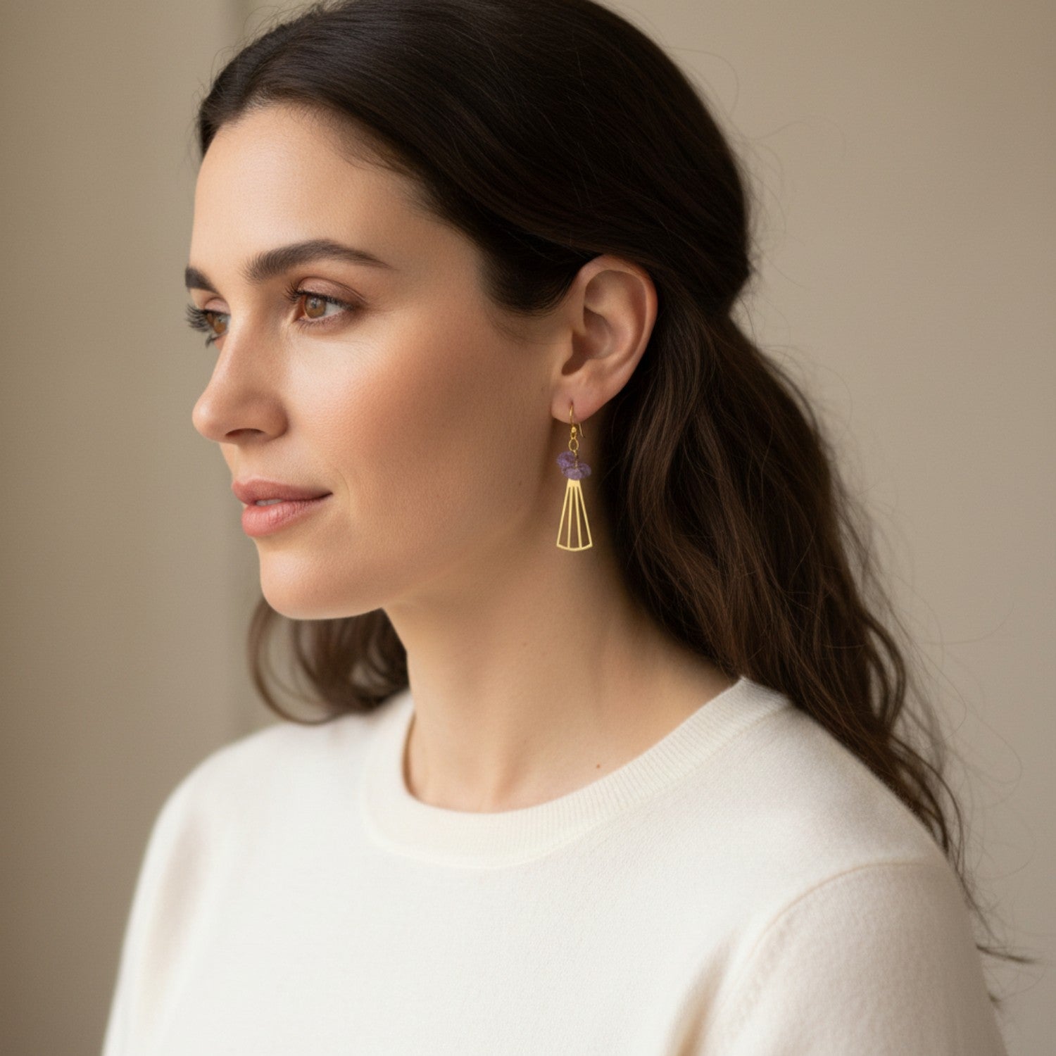 Woman wearing gold earrings with amethyst with a neutral background
