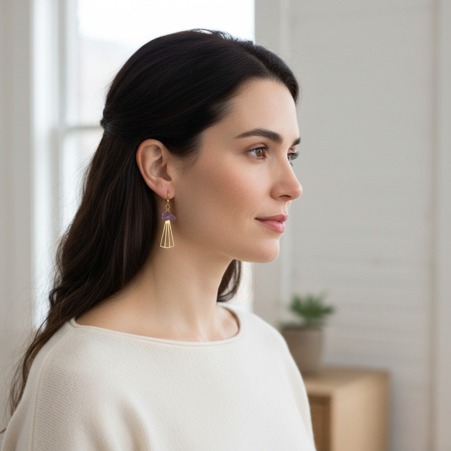 Woman wearing gold earrings with amethyst stones in a blurred indoor background