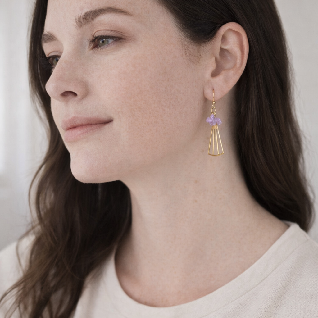 Close-up of a woman wearing gold earrings with amethyst stone against a neutral background