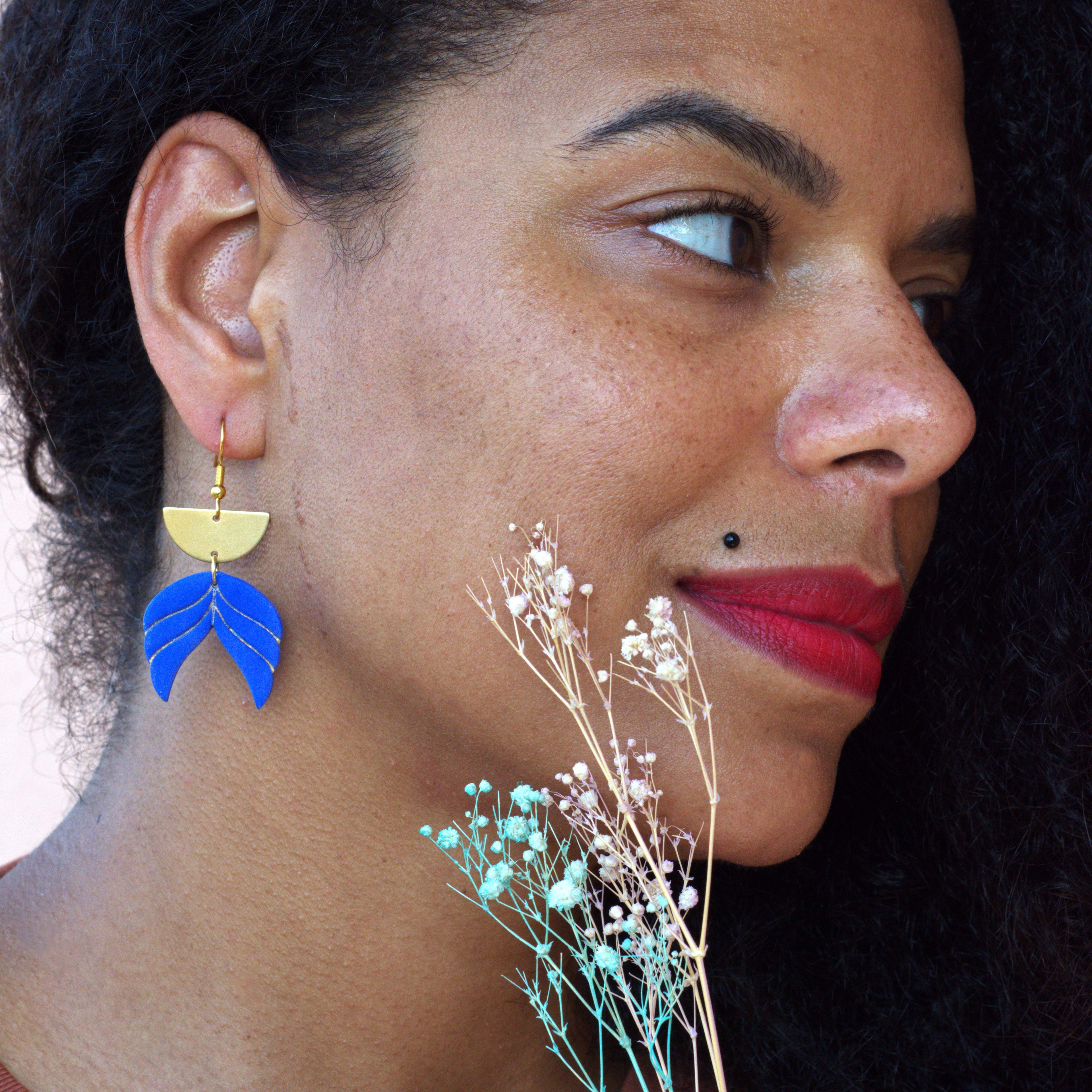 Model wearing handmade blue polymer clay leaf drop earrings with gold-plated hooks, lightweight geometric statement earrings shown in profile.