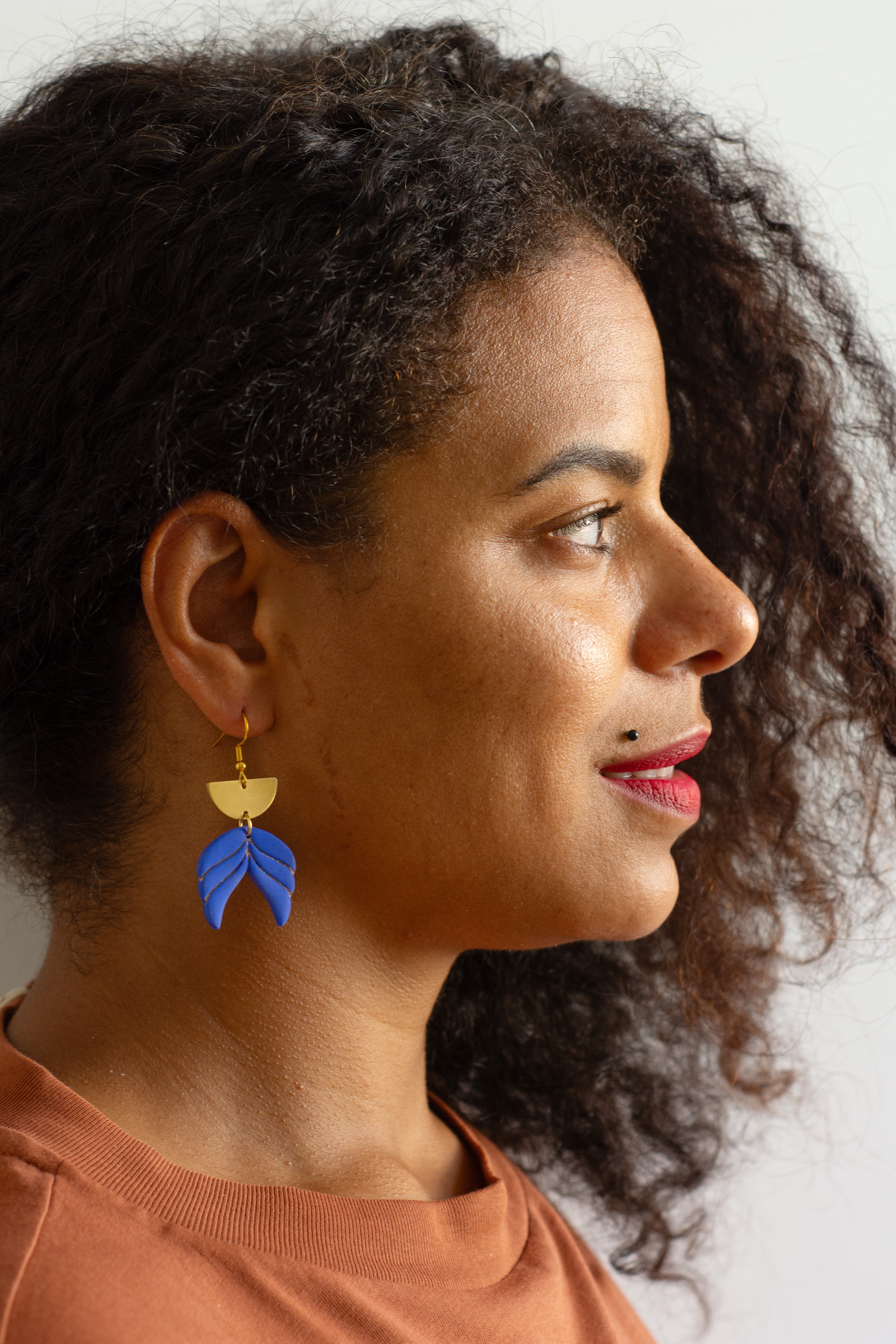 Model wearing handmade blue polymer clay leaf drop earrings with gold-plated hooks, lightweight geometric statement earrings shown in profile.