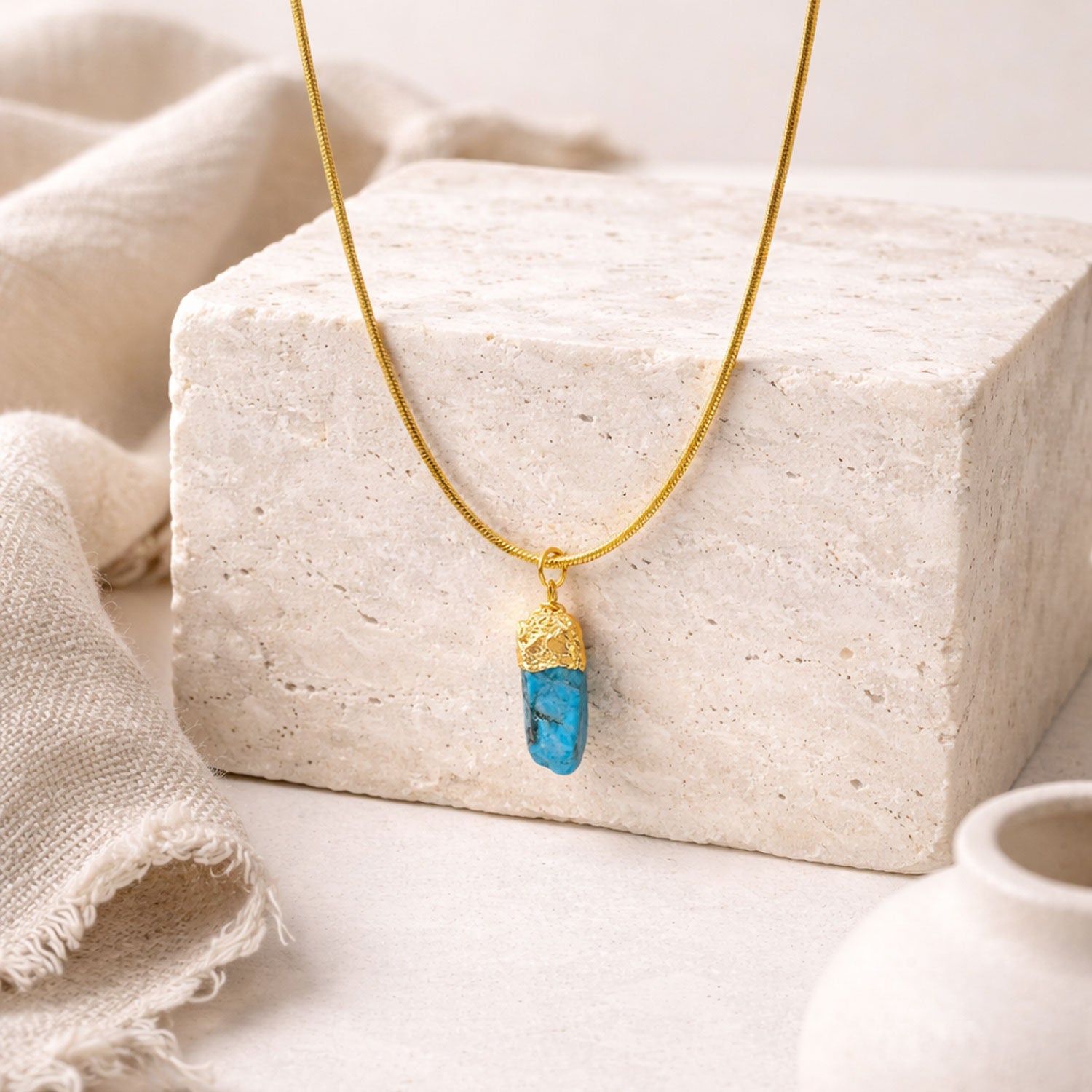 Gold necklace with a blue apatite pendant on a textured surface