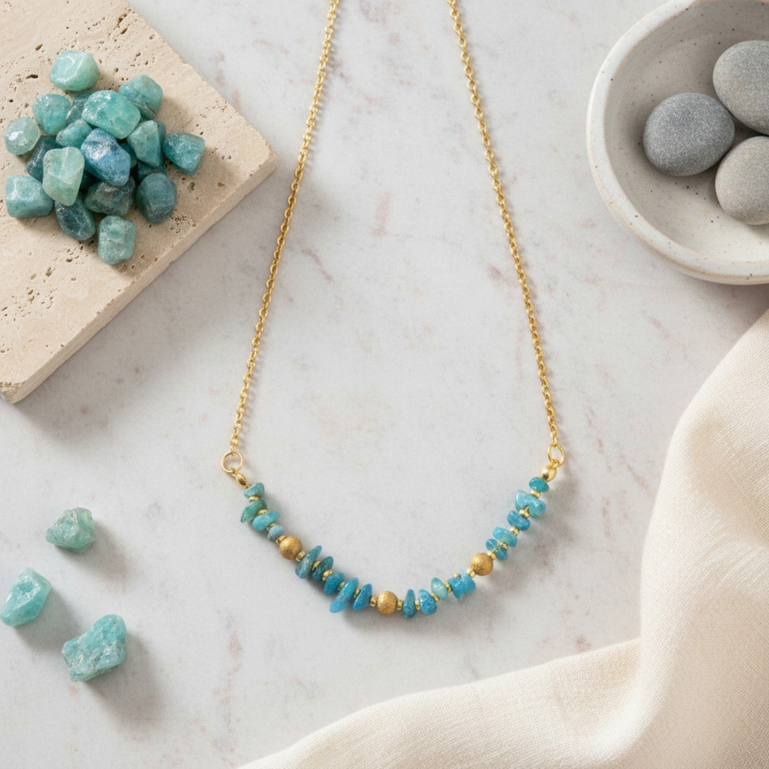 Turquoise beaded necklace on a marble surface with stones and a bowl.
