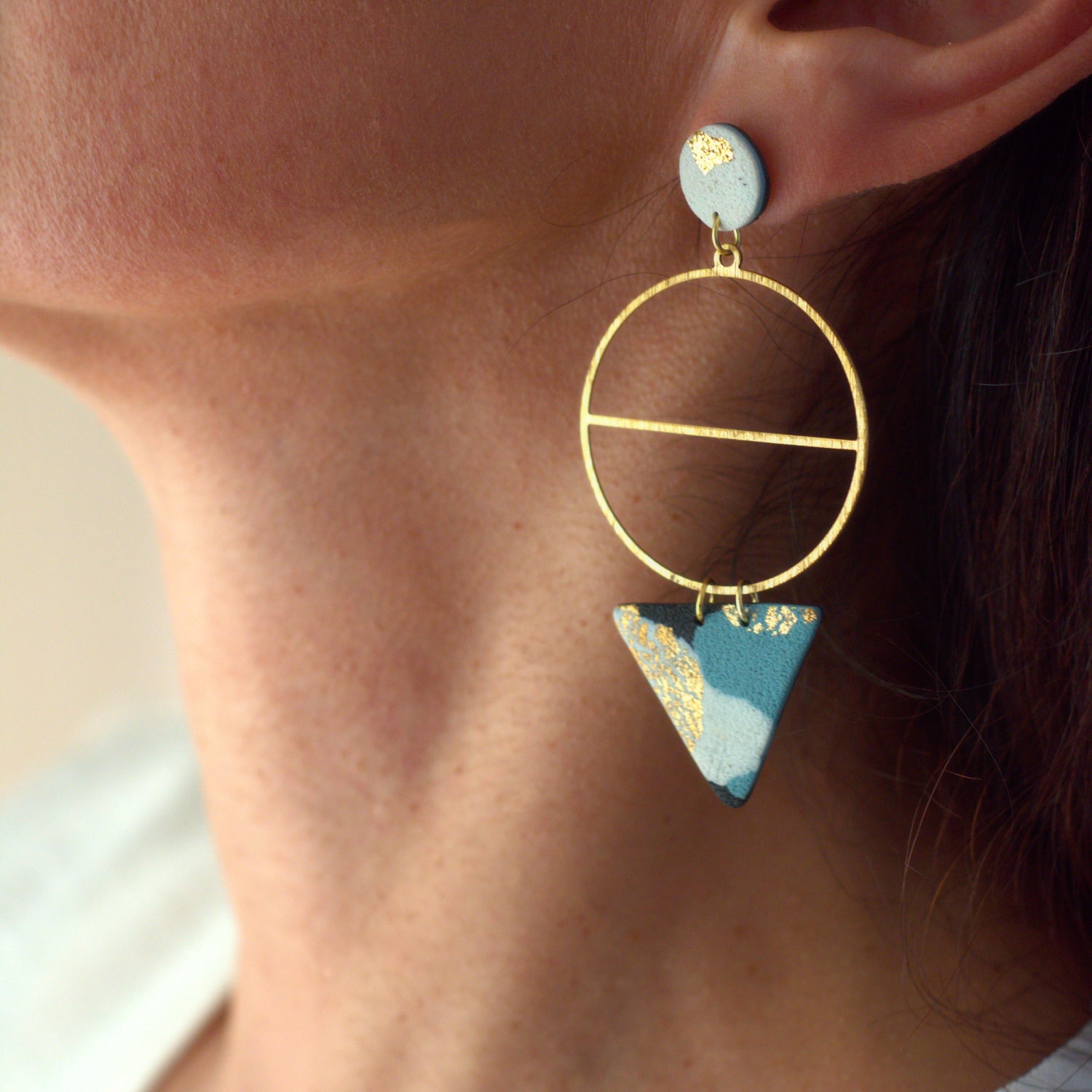 Close up fo a Gold hoop earring with a blue triangle pendant worn by a woman.
