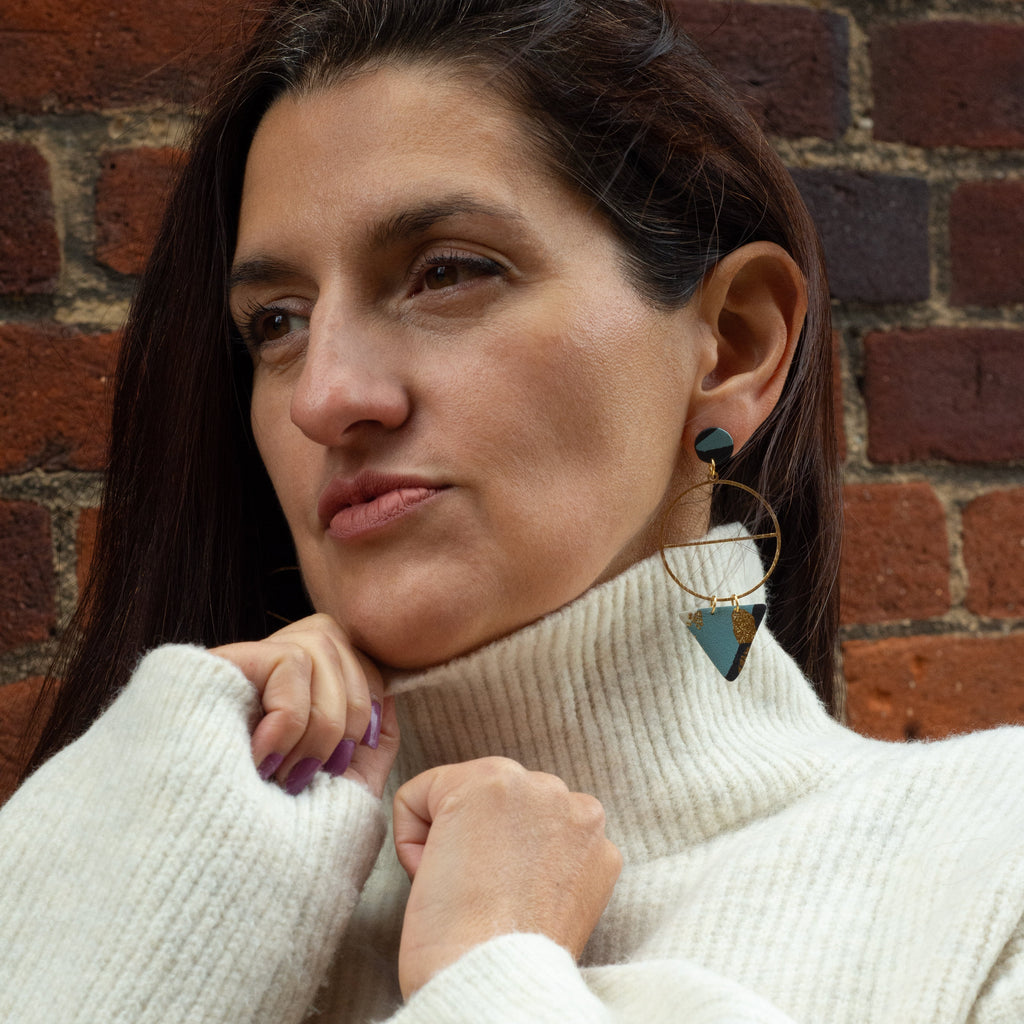 Woman wearing a white turtleneck sweater against a brick wall and wearing blue and black earrings