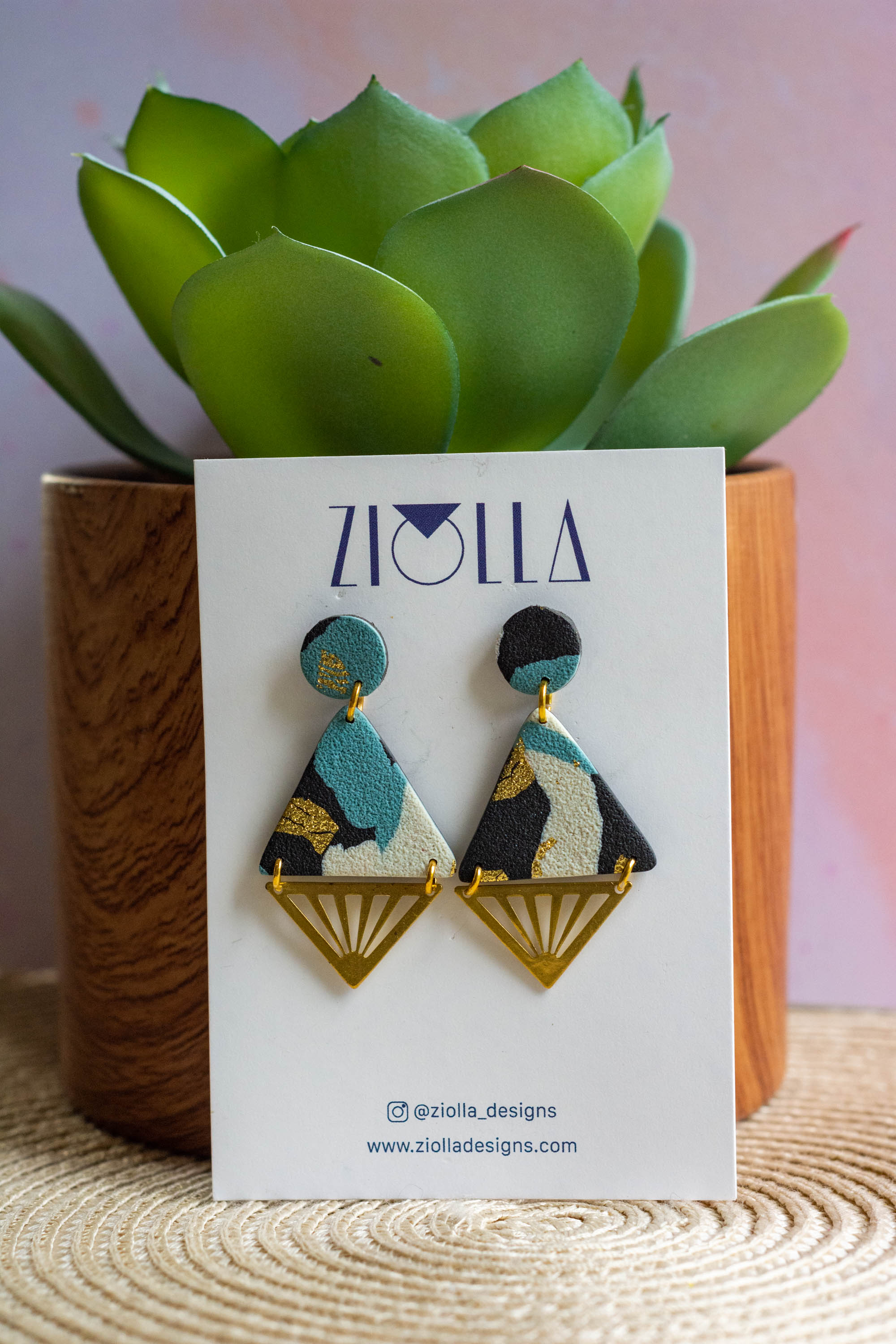 Handmade geometric statement earrings by Ziolla Designs, featuring brass triangles with marbled teal, black and gold polymer clay details, displayed on a branded jewellery card.