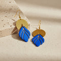 Pair of earrings with blue and gold design on a beige surface