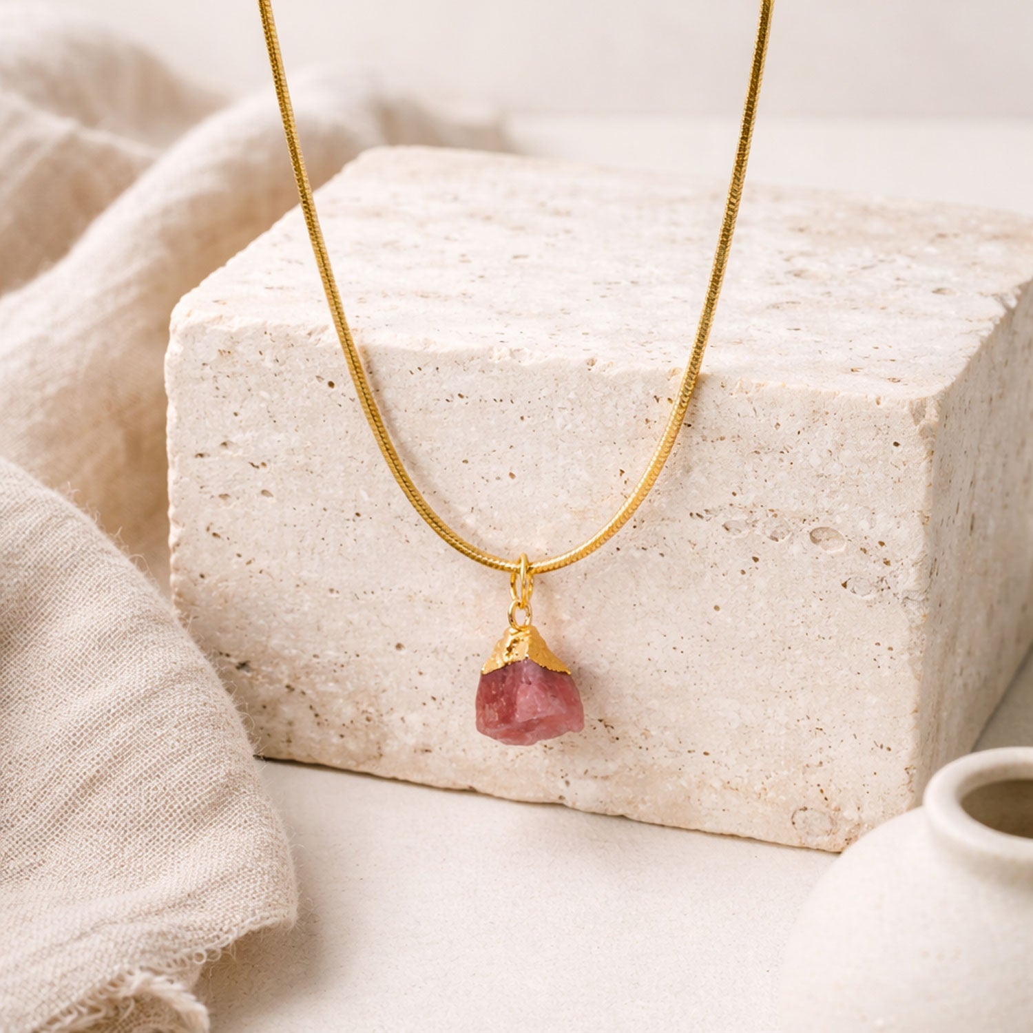 Gold necklace with a rose quartz gemstone pendant on a textured surface