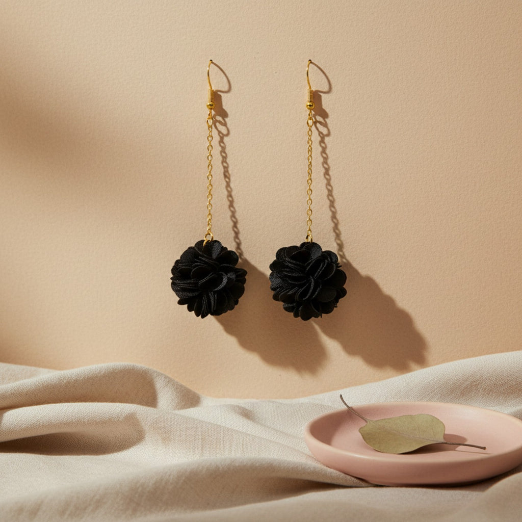 Black floral earrings with gold chains on a beige background