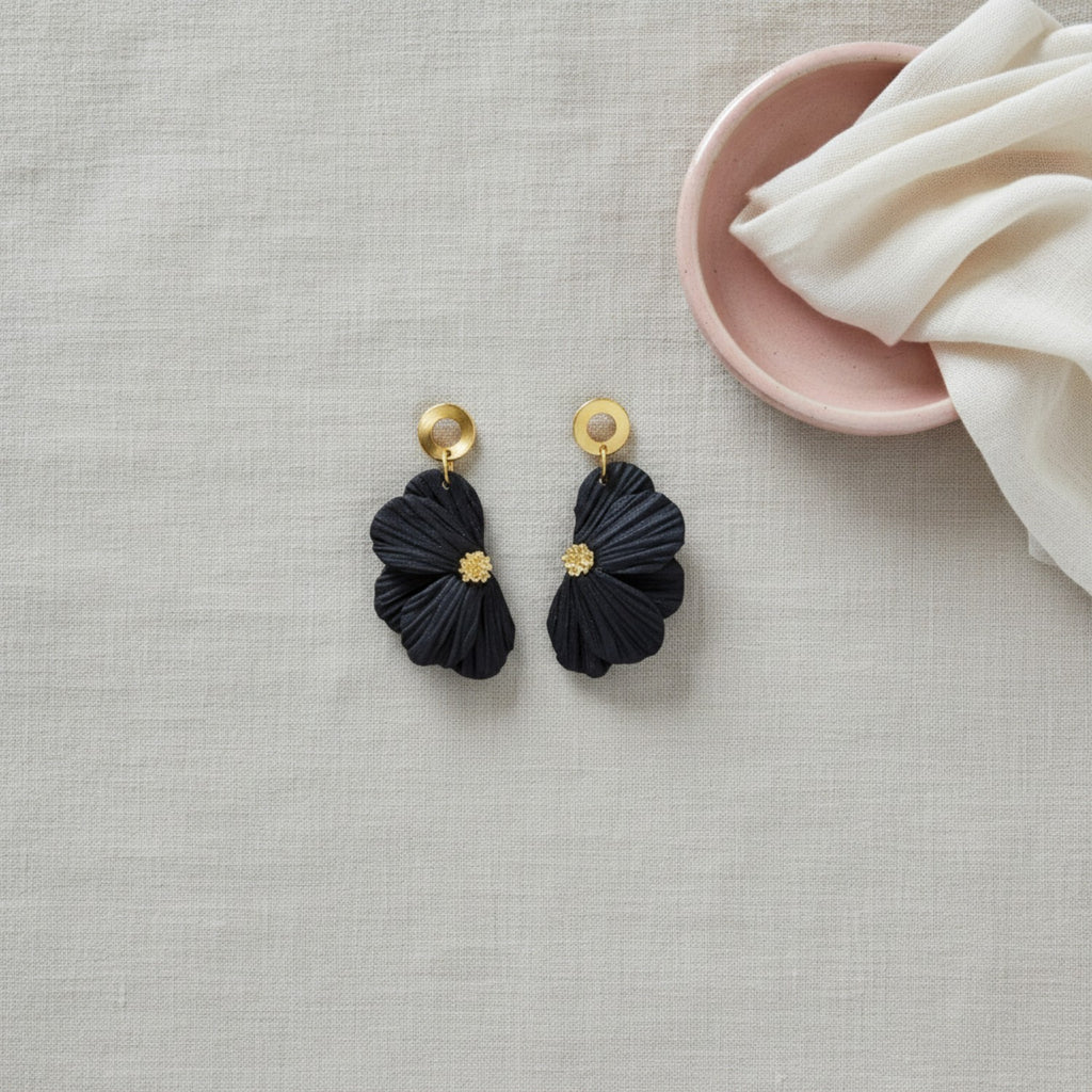 Black flower earrings with gold pistils on a white stand against a beige background
