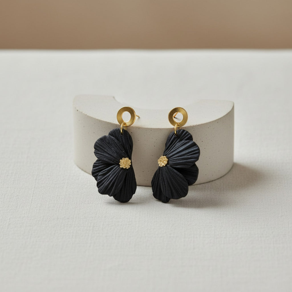 Black flower earrings with gold pistils on a white stand against a beige background