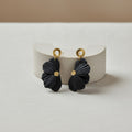 Black flower earrings with gold pistils on a white stand against a beige background