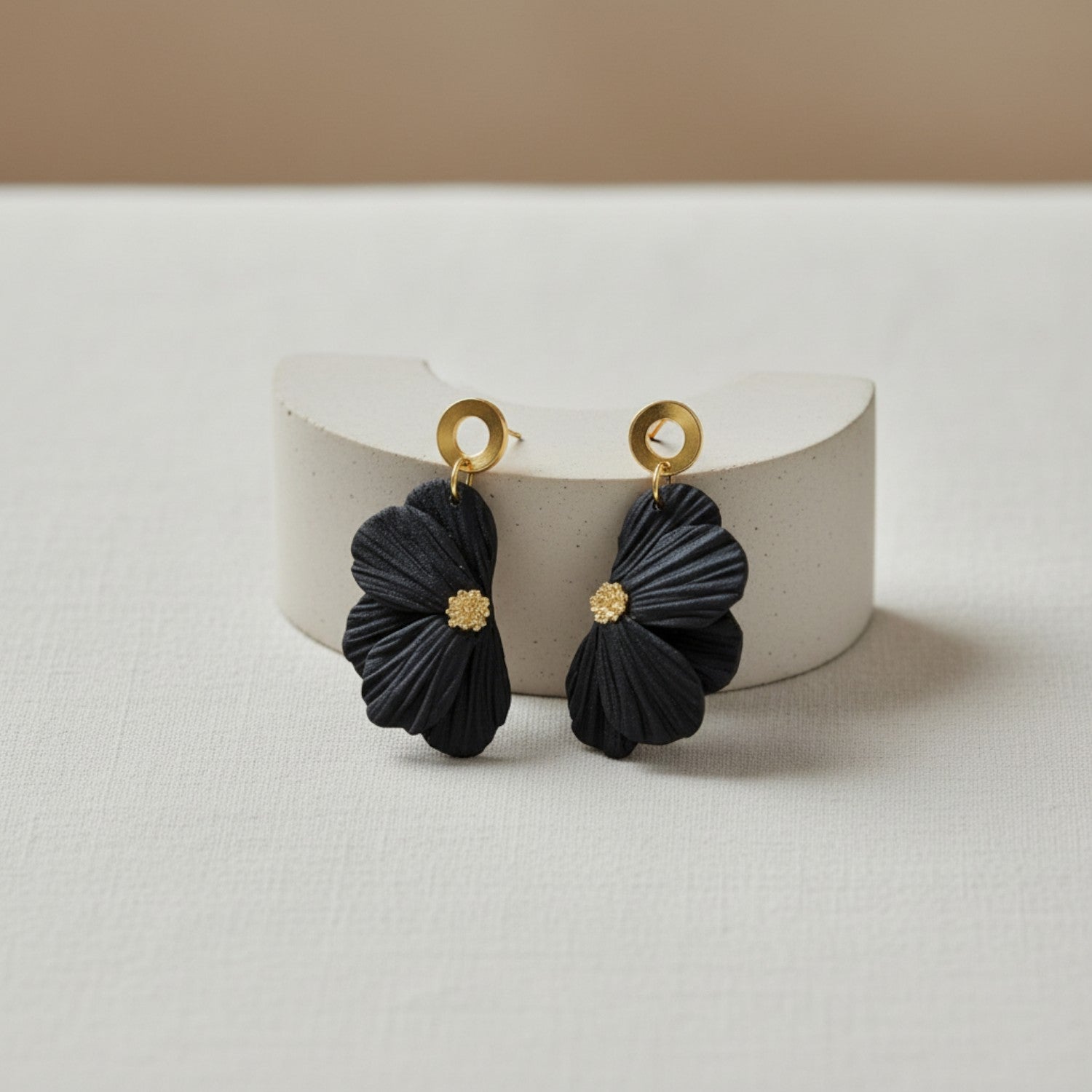 Black flower earrings with gold pistils on a white stand against a beige background