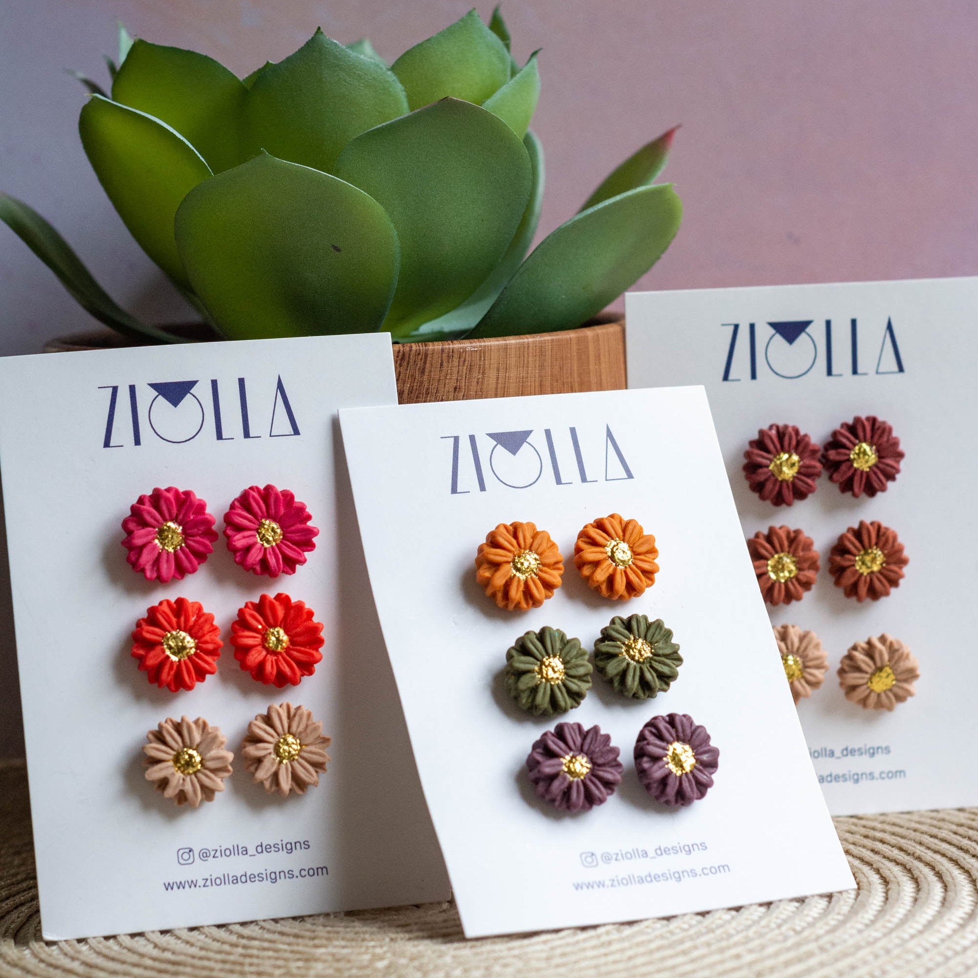 Flower earrings displayed on cards with a plant in the background