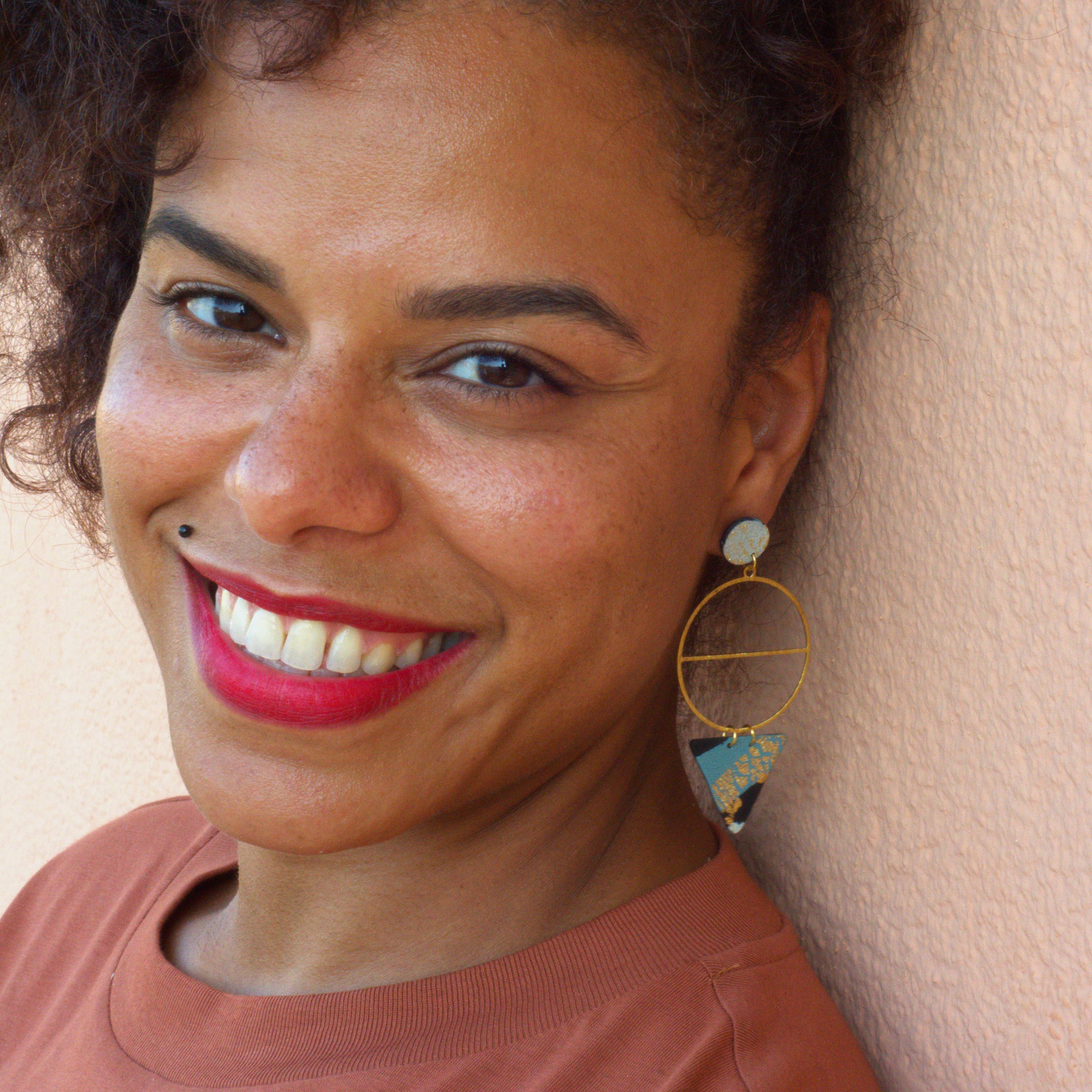 Woman wearing black and blue earrings against a beige wall