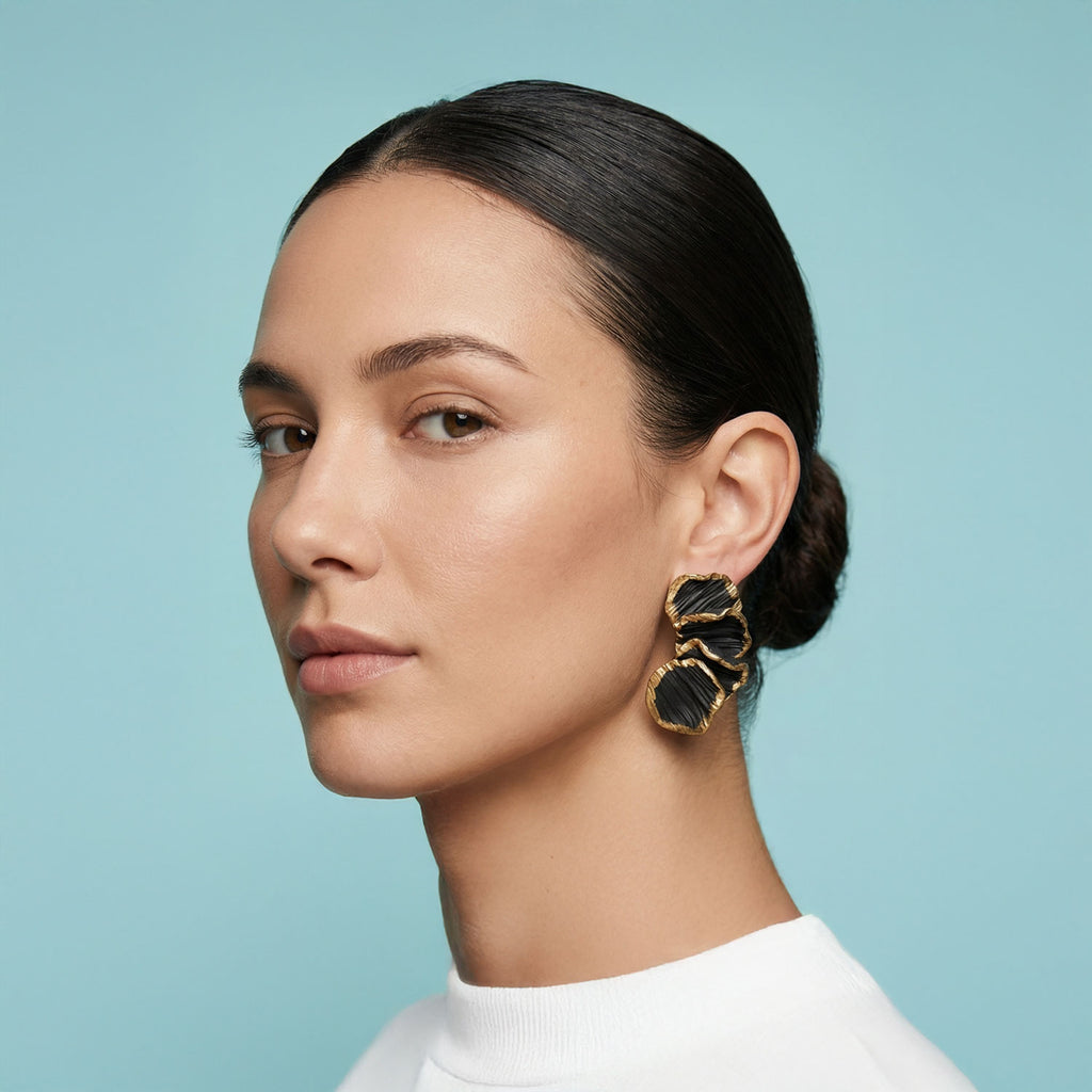 Woman wearing gold and black earrings against a light blue background