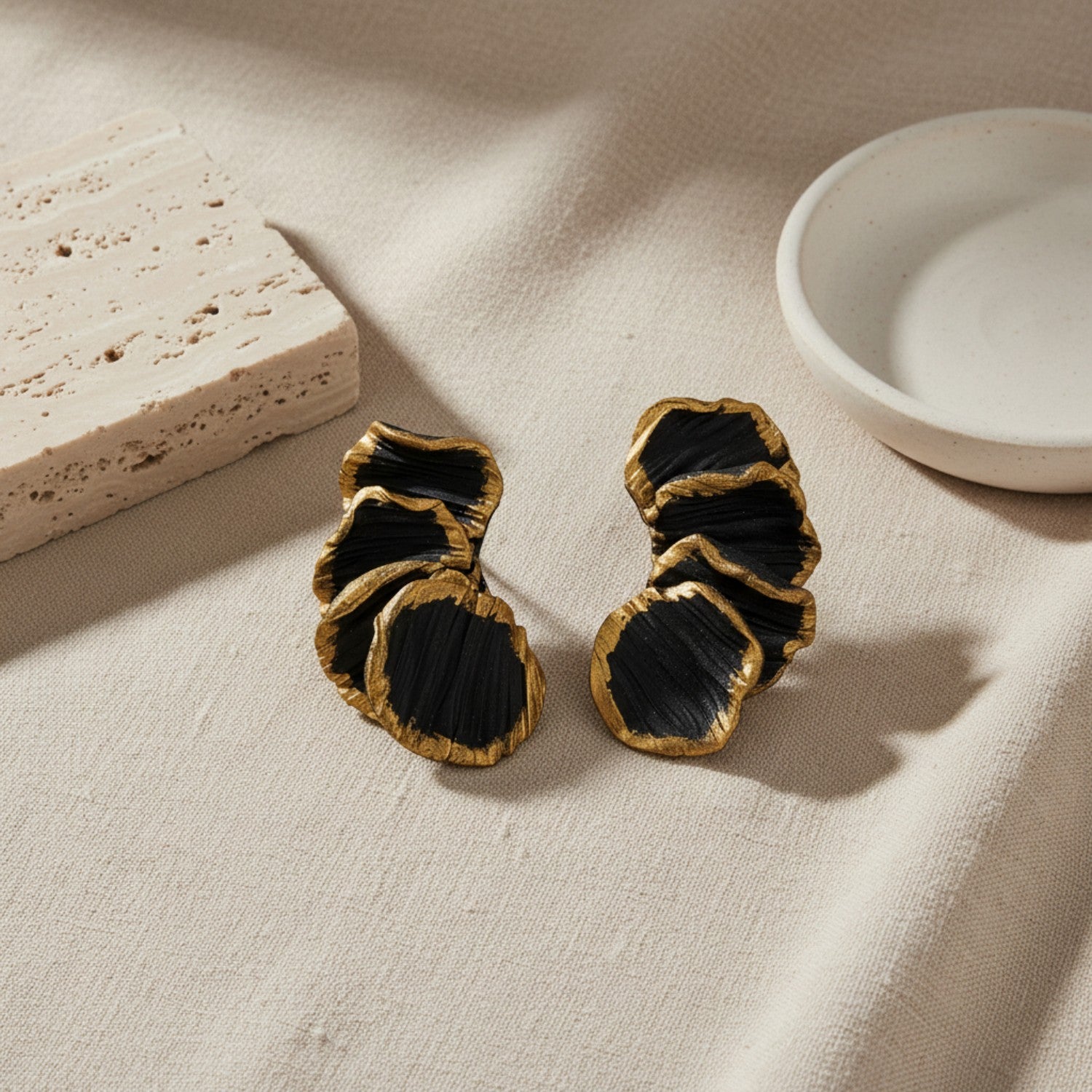 Black and gold earrings on a beige fabric surface