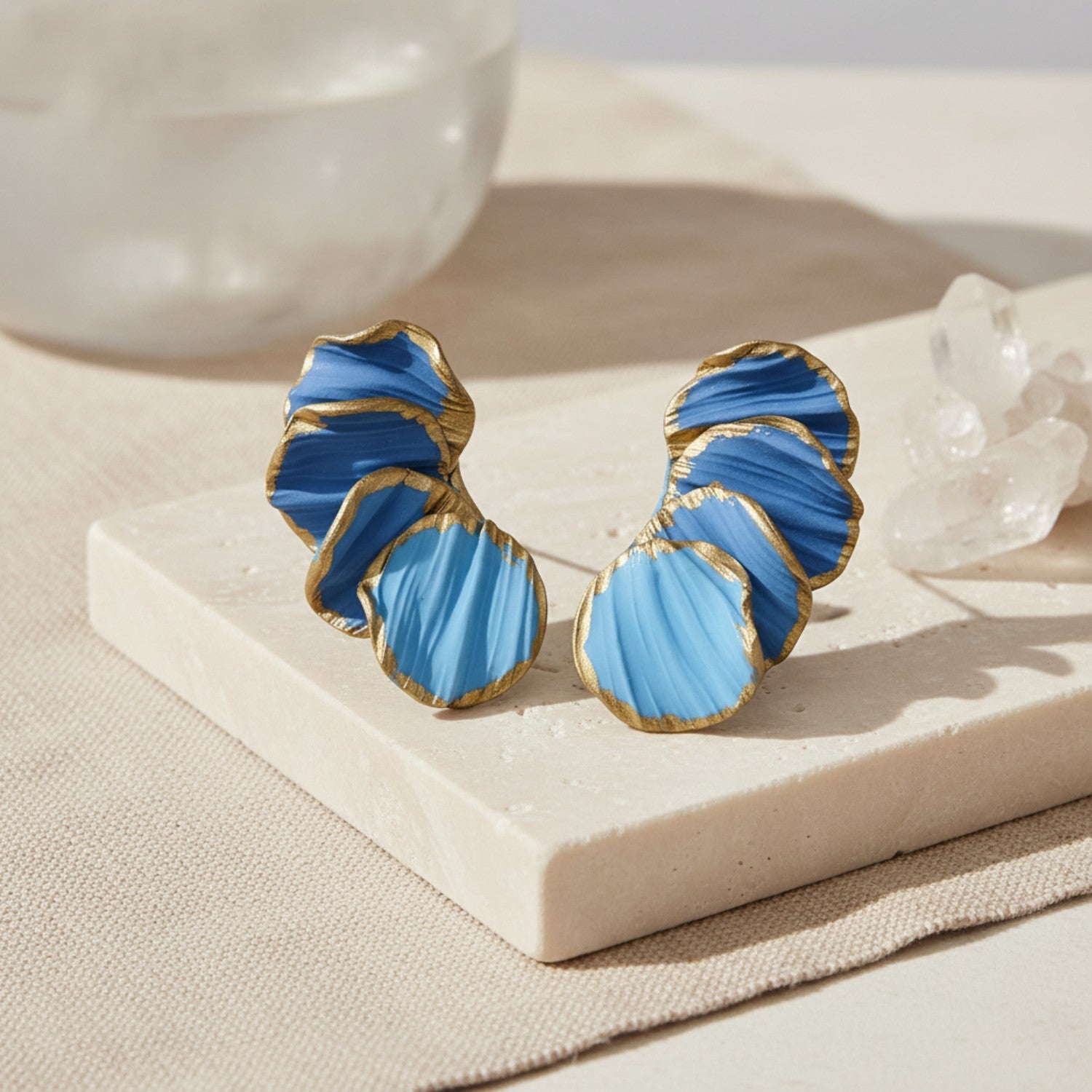 Blue and gold earrings on a white stone surface with a neutral background