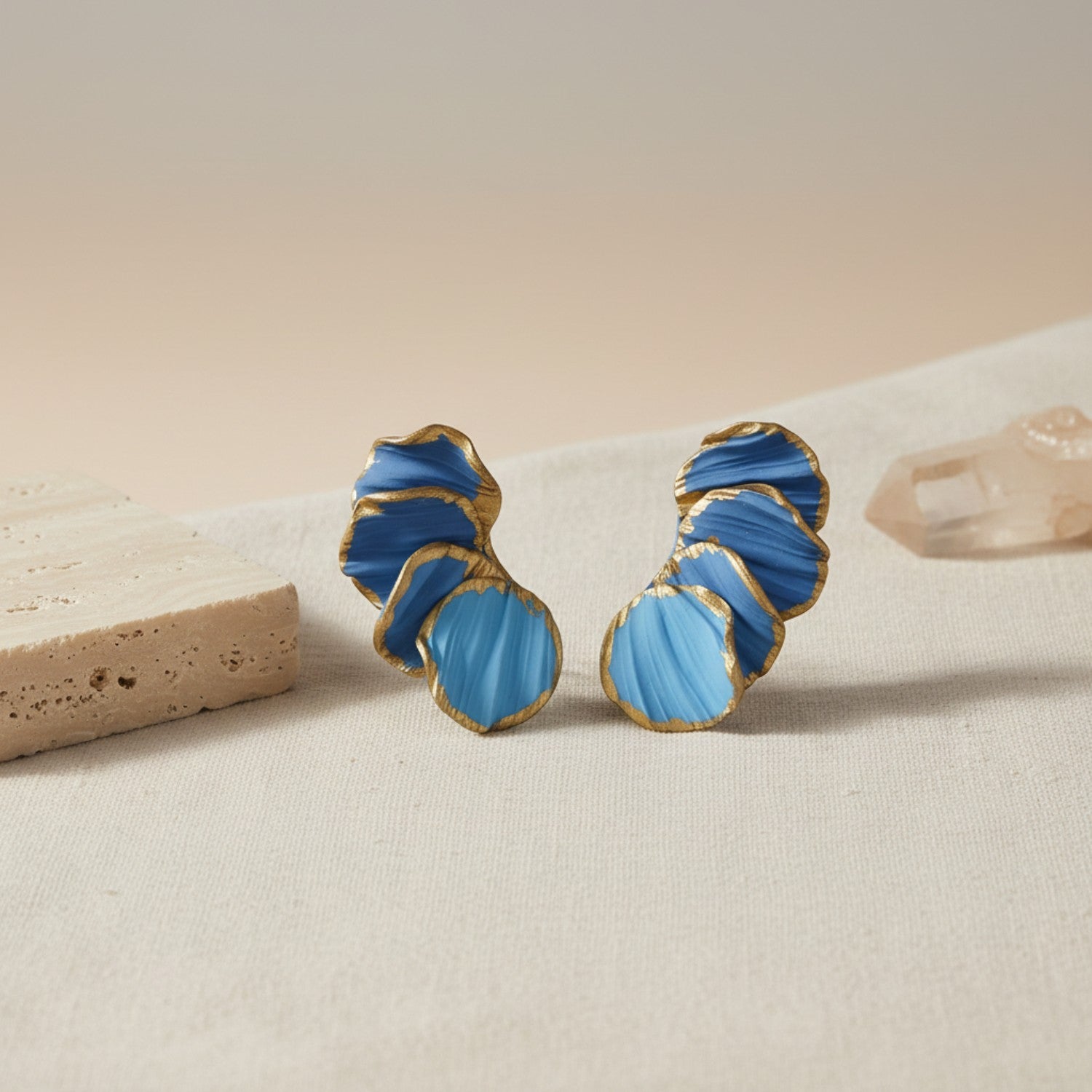Blue and gold earrings on a beige surface