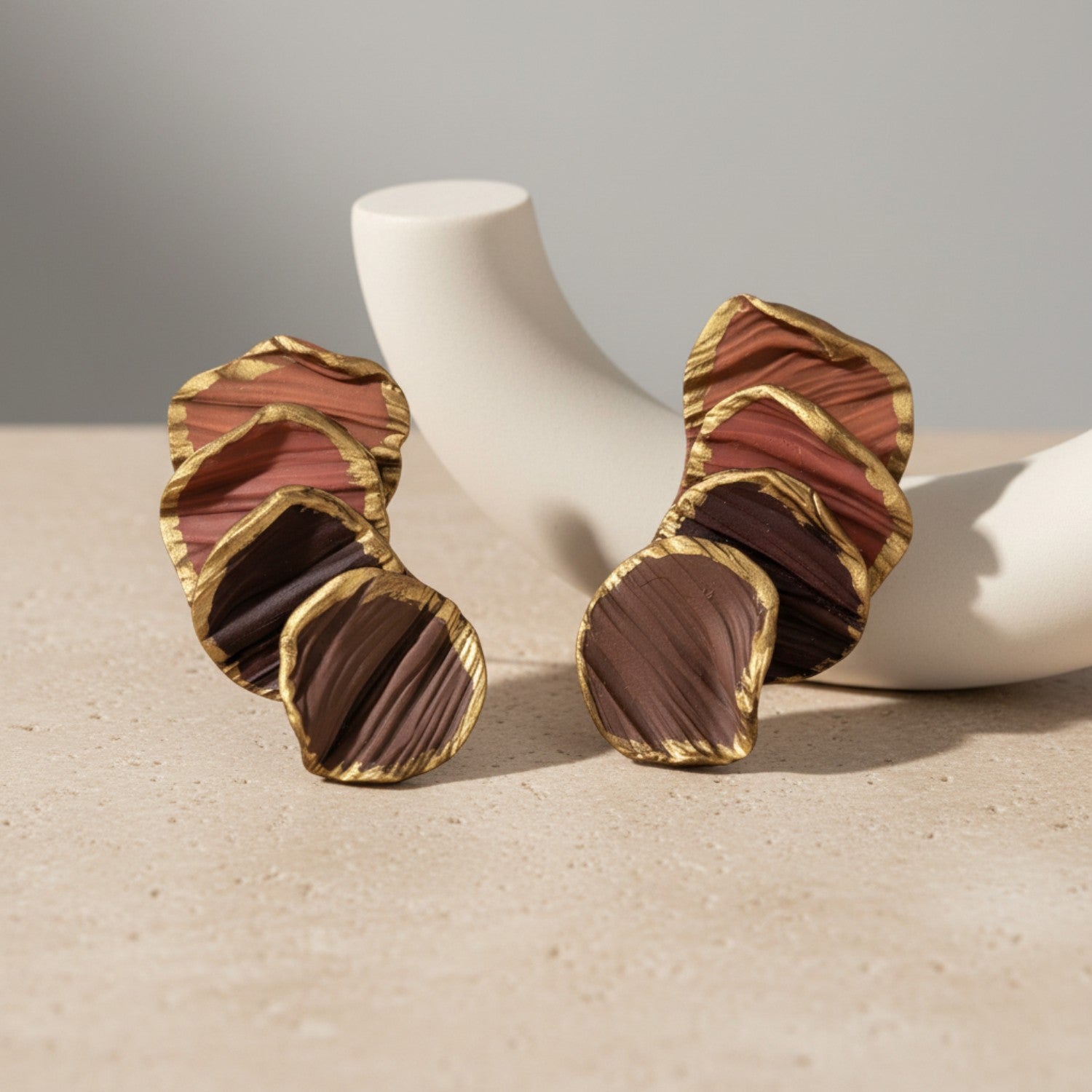 Pair of gold and brown earrings on a beige surface with a neutral background