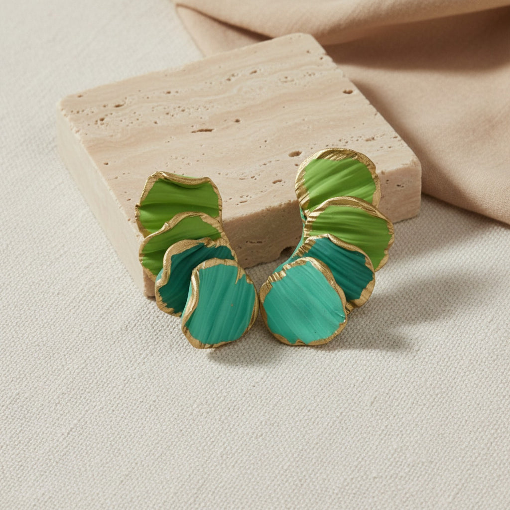Green and gold earrings on a beige stone surface
