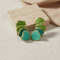 Green and gold earrings on a beige stone surface