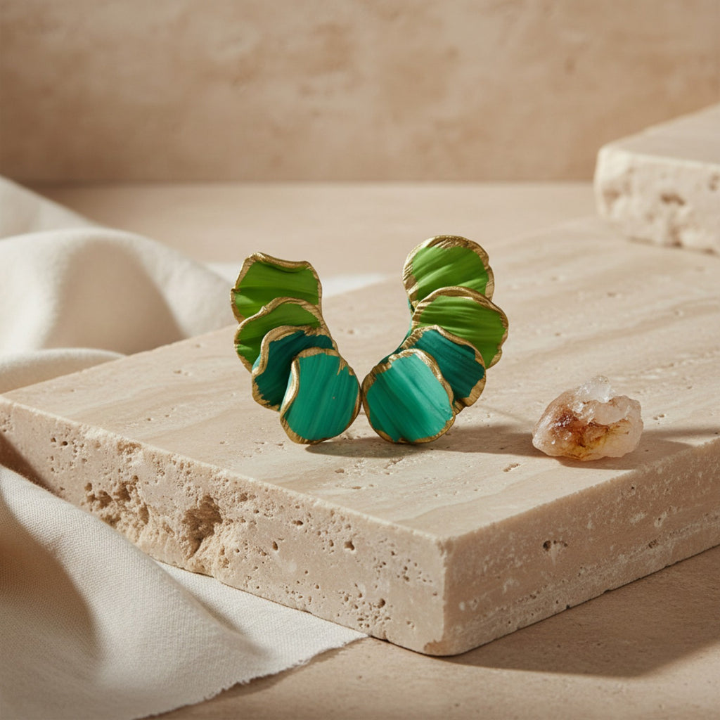 Green leaf-shaped earrings on a beige stone surface with a soft background