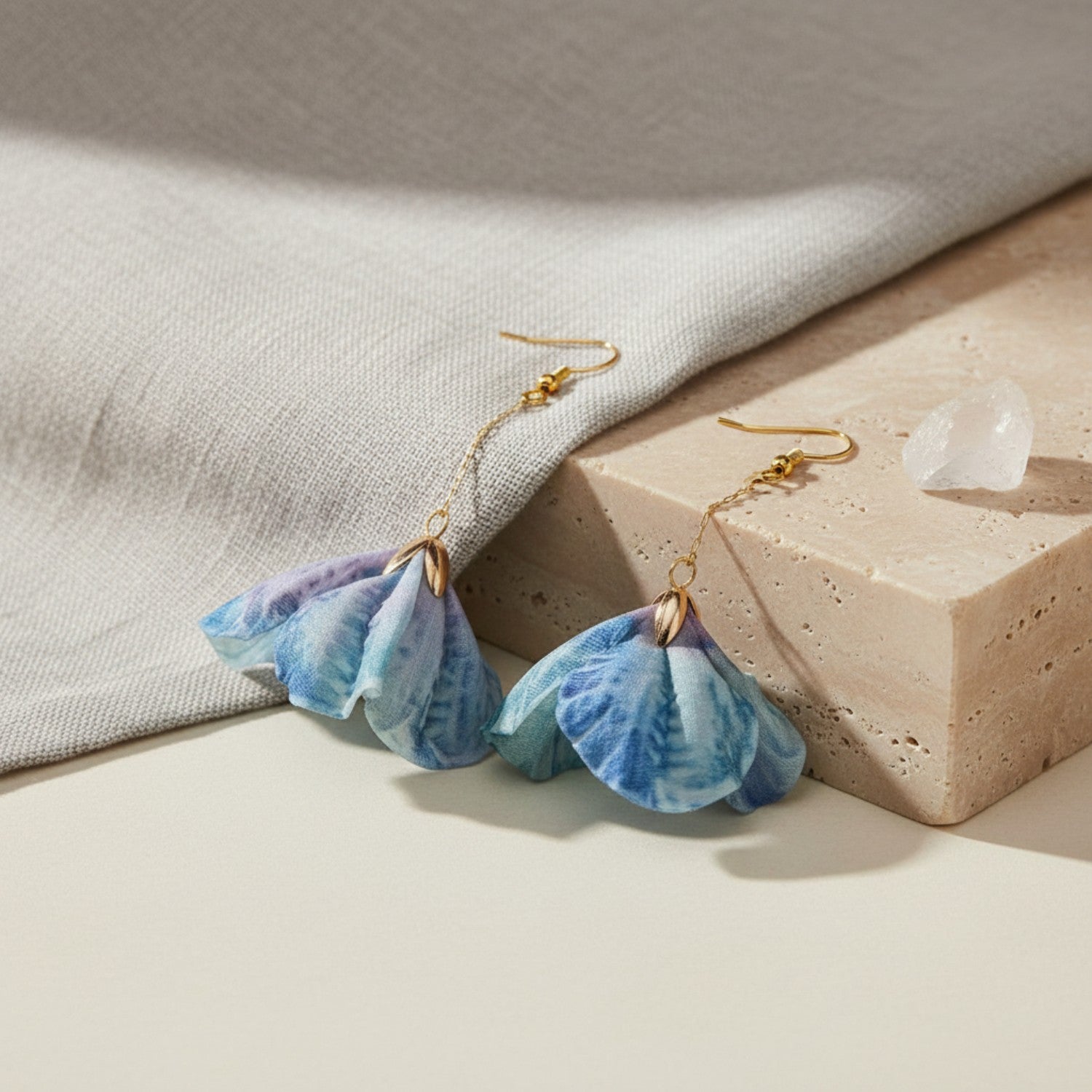 Blue and purple earrings emulating flowers on a neutral background