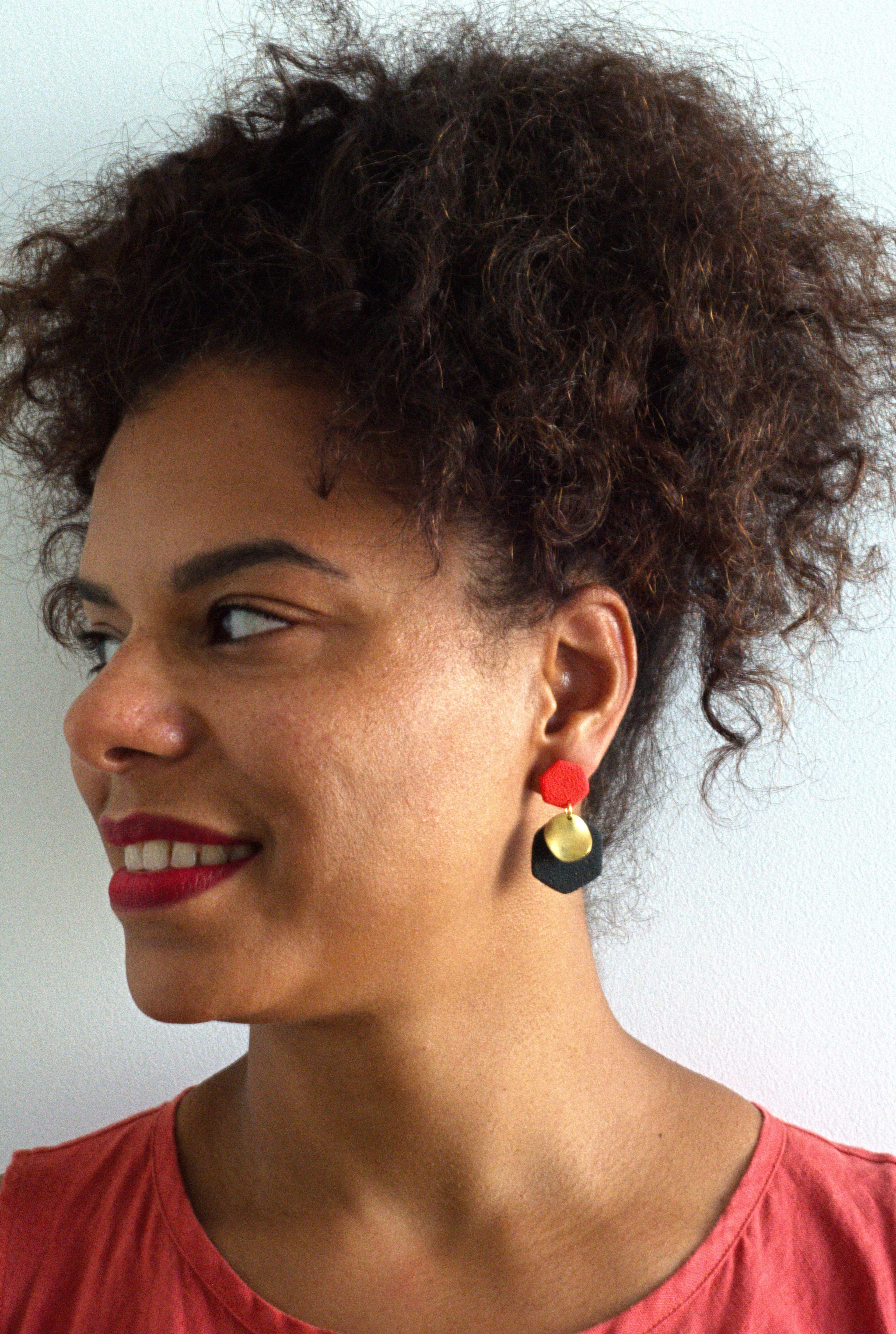 Woman with hair up wearing a pair of black and orange earrings with a brass charm