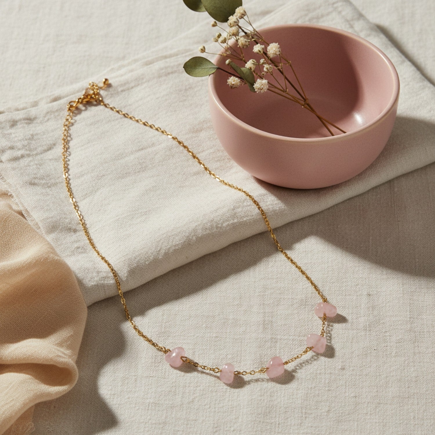 Rose quartz five-bead necklace displayed on neutral fabric with a pink ceramic bowl and raw rose quartz crystal.