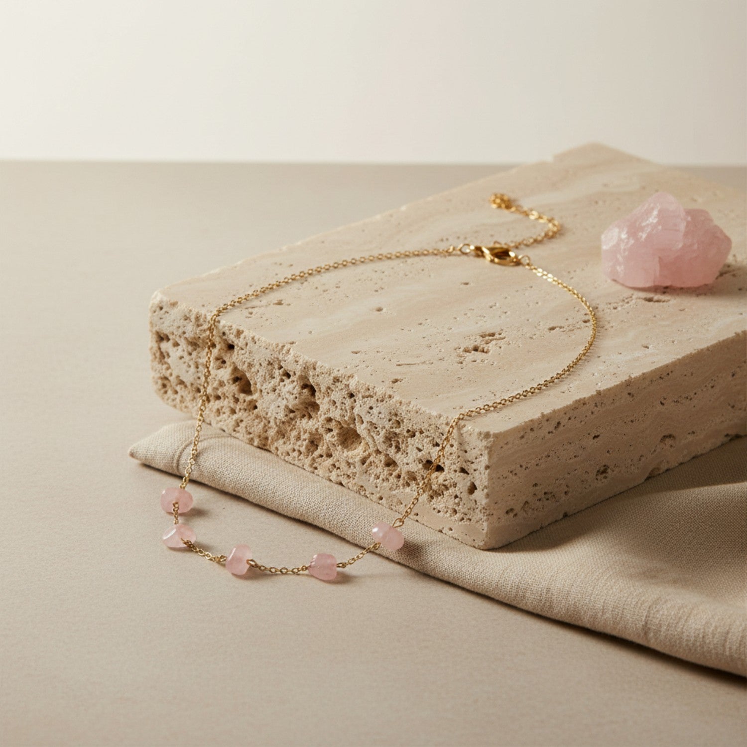 Minimalist flat lay of a rose quartz five-bead necklace on a light stone surface, showing gold chain and soft pink beads.