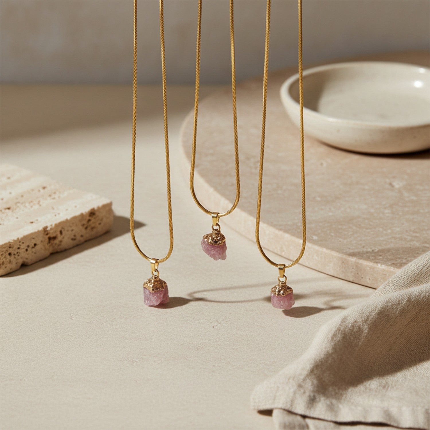 Three gold necklaces with rose quartz pendant drops on a neutral background