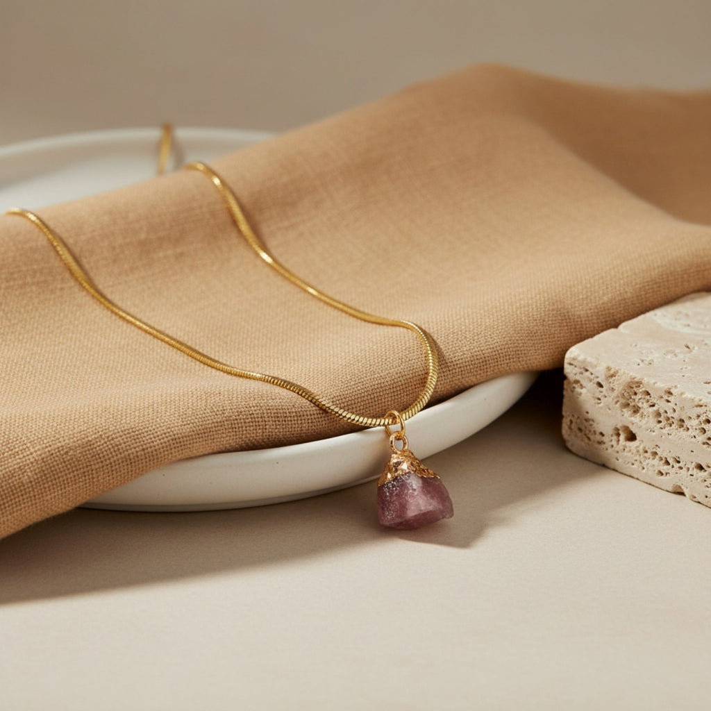 Gold necklace with a rose quartz pendant on a beige napkin and plate