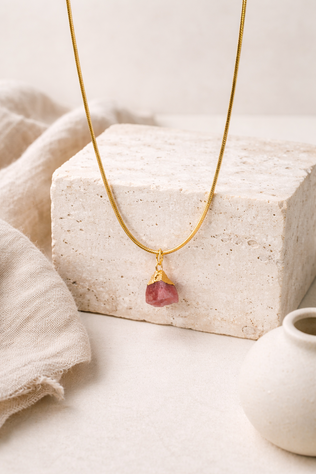 Gold necklace with a rose quartz gemstone pendant on a neutral background