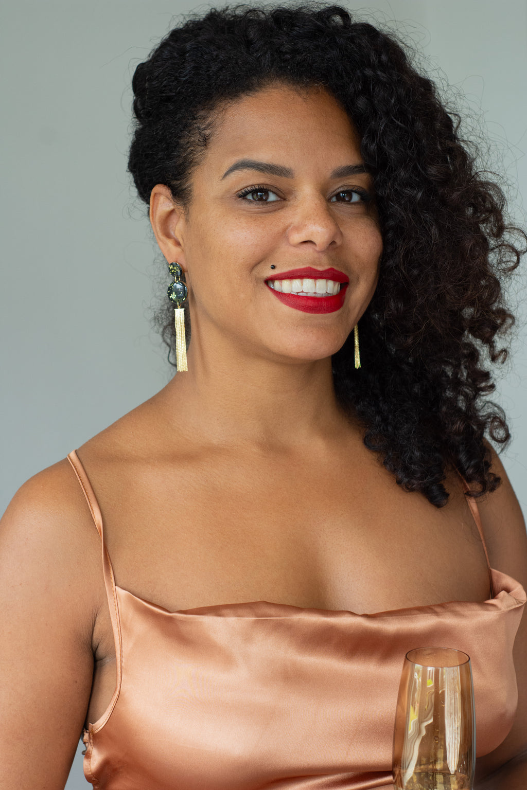 Model wearing handmade black and gold tassel drop earrings with speckled polymer clay discs and gold-plated chain fringe, elegant statement earrings shown in profile.
