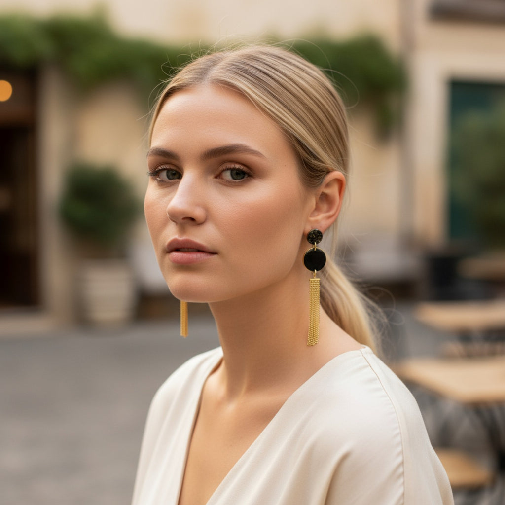 Model wearing handmade black and gold tassel drop earrings with speckled polymer clay discs and gold-plated chain fringe, elegant statement earrings shown in profile.