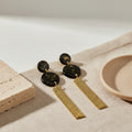 Black and gold earrings  with tassels on a beige surface with a neutral background