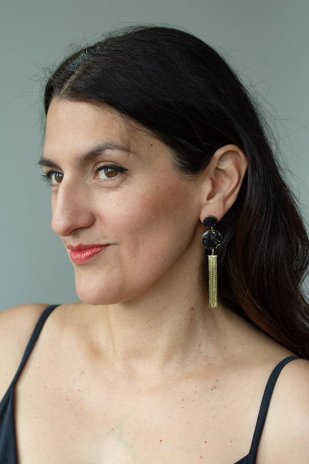 woman smiling wearing a pair of black and gold earrings with golden tassels