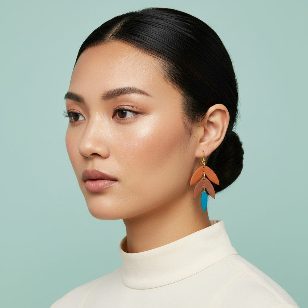 Woman wearing oreange and blue tiered earrings against a light blue background