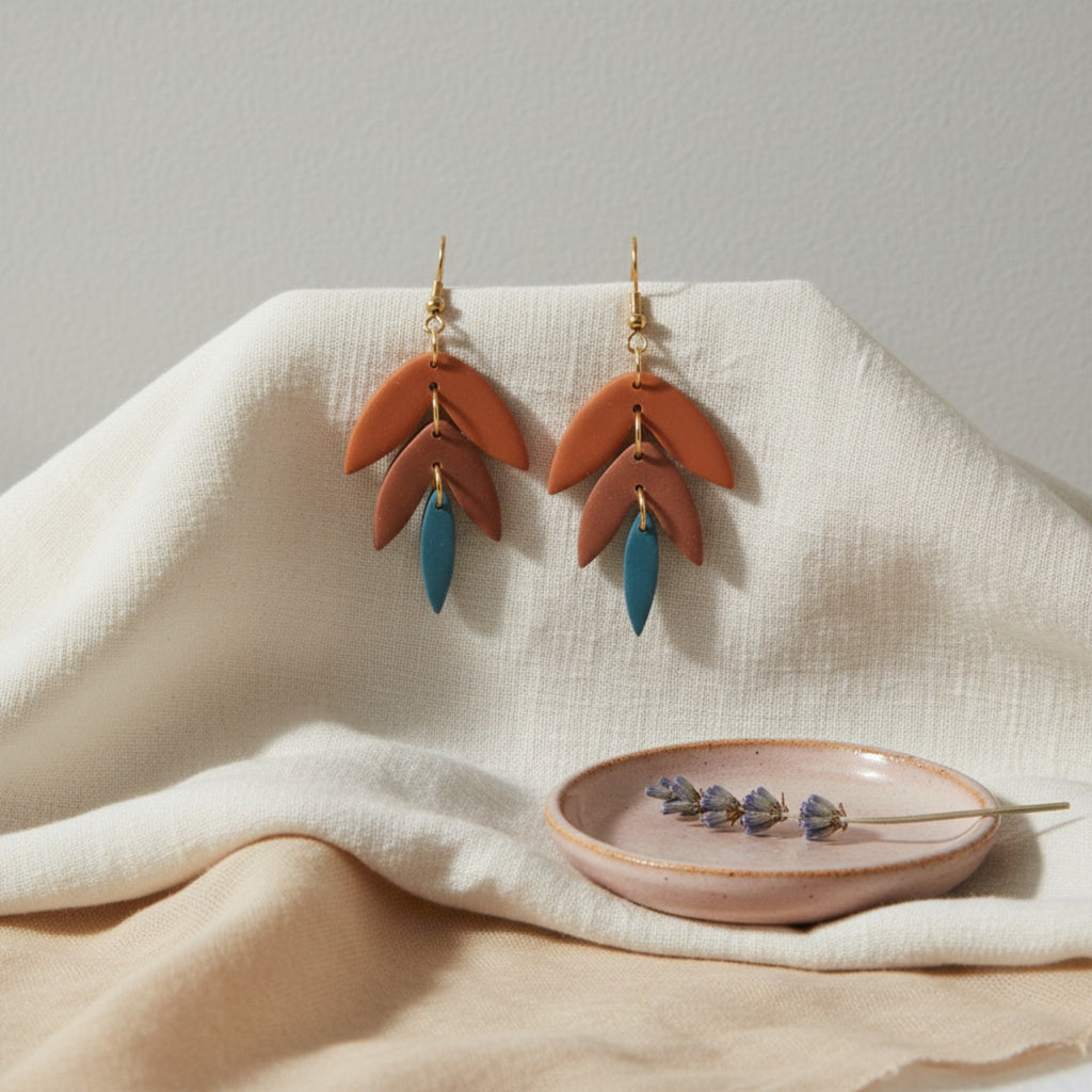 Pair of oreange and blue tiered earrings with terracotta and blue leaf-like designs on a beige fabric background.