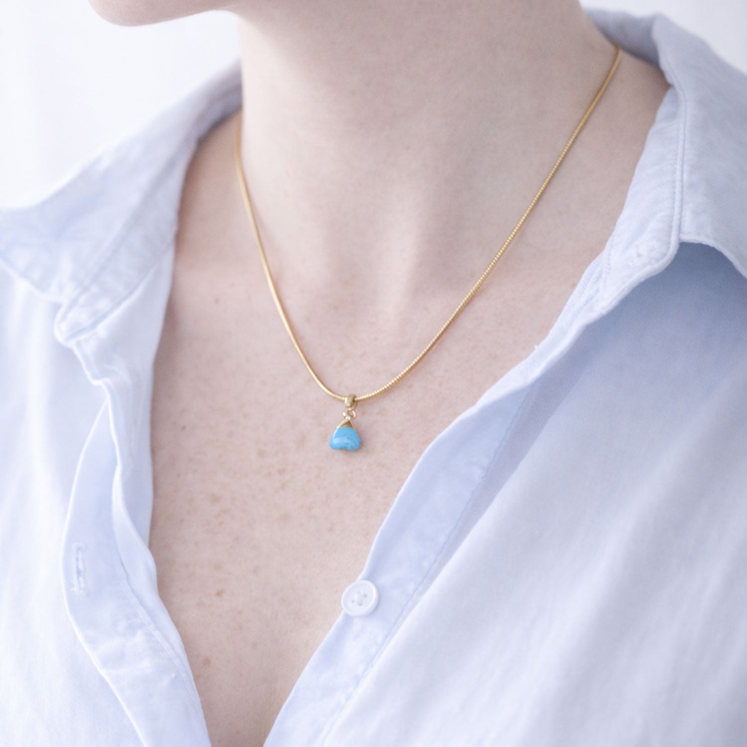Necklace with a turquoise pendant worn by a person in a white shirt