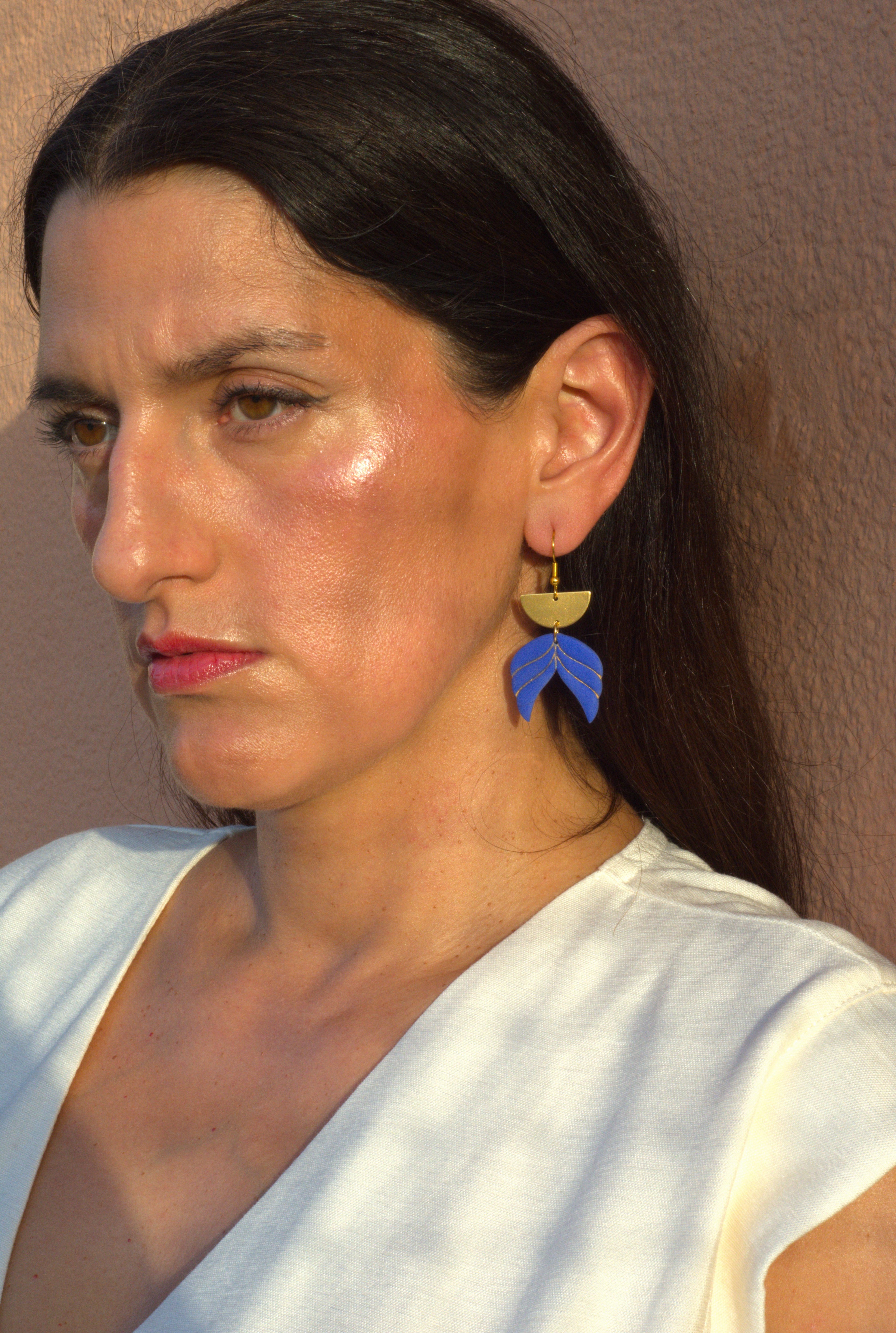 Model wearing handmade blue polymer clay leaf drop earrings with gold-plated hooks, lightweight geometric statement earrings shown in profile.