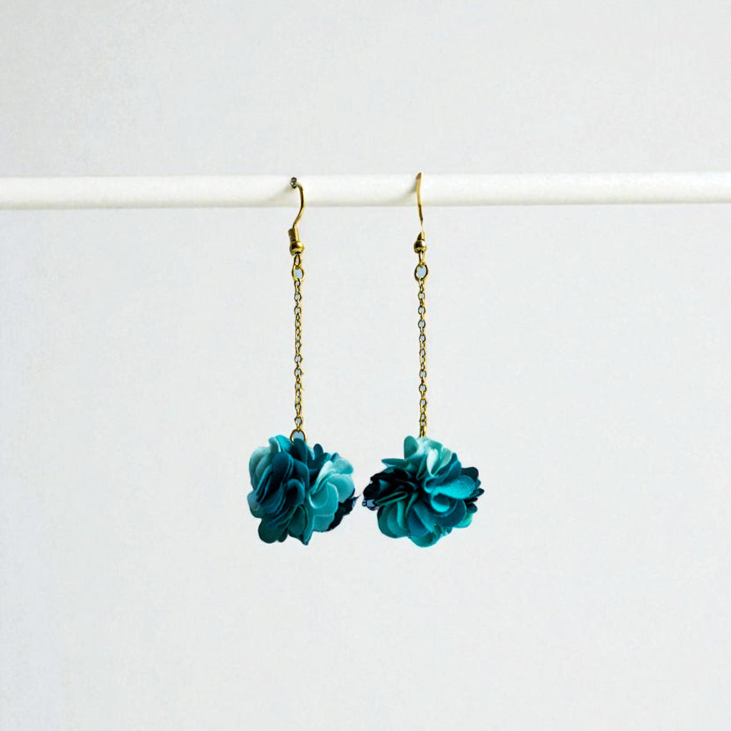 Teal flower earrings on gold chains against a white background